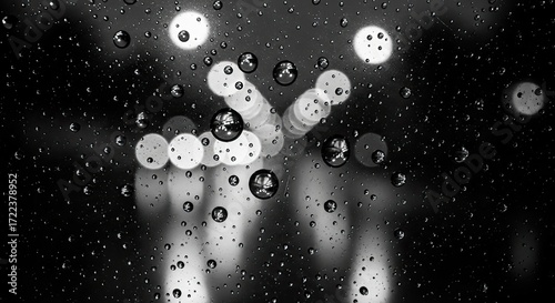 Abstract view of raindrops on a window at night, blurred city lights visible through the water droplets.