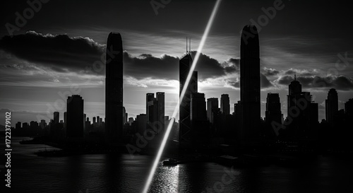Dramatic black and white Hong Kong skyline at sunset, sun ray piercing clouds.
