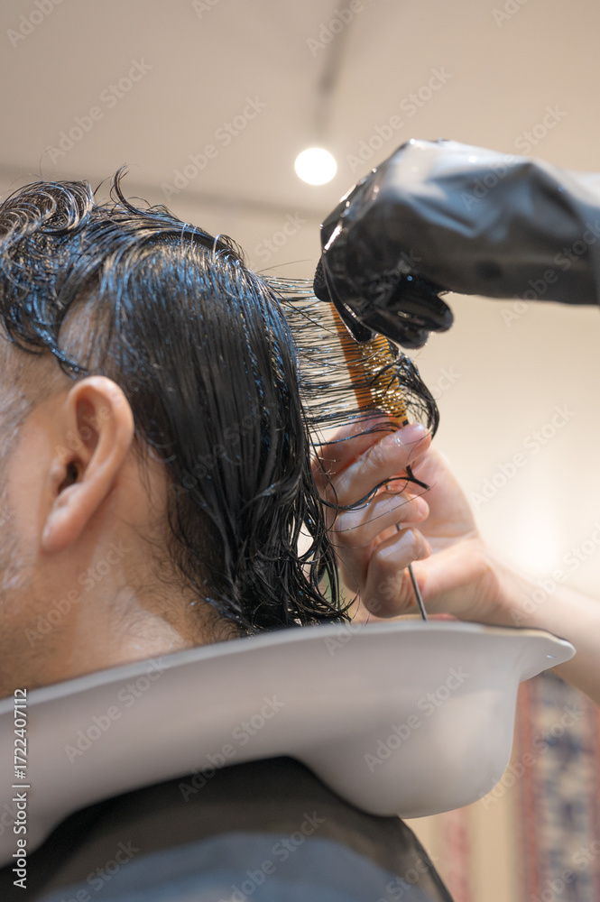 Naklejka premium Close-up of a man's hands as he performs a perm treatment at a hair salon