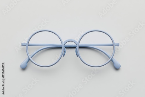 Light blue round glasses on a pale surface. A centered close-up features thin, round eyewear with a minimalist, airy aesthetic