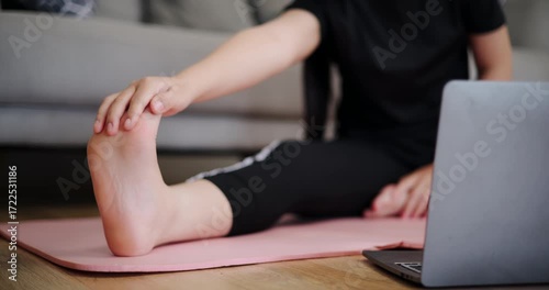 Handheld selective focus shot, Young Asian woman practicing stretching online on laptop in living room at home. Healthy lifestyle. Women Lifestyle