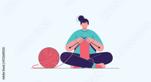 A person is sitting cross legged and knitting a red garment with a large ball of pink yarn beside them.