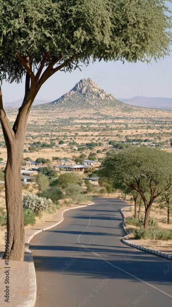 Obraz premium Scenic Road Through Arid Landscape with Mountain Backdrop, Village, and Trees