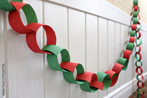 Colorful paper chain garland in red and green interlocking circles hanging along white wainscoting for cheerful holiday decor.