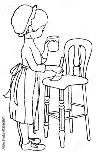 Adorable child in apron happily painting a wooden high chair with a brush and pot creating delightful artwork