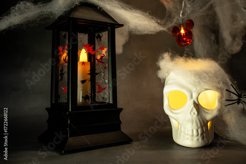 Skull with glowing yellow eyes sits amid cobwebs and a black spider, casting warm light against a dark background. A classic Halloween setup creating a spooky, eerie, and festive atmosphere.
