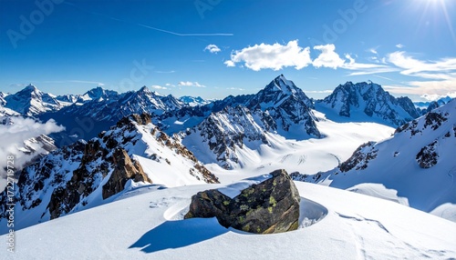 Stunning snowy mountain range vista with blue sky and wispy clouds, a lone rock foreground, pristine white snow, and breathtaking scenery