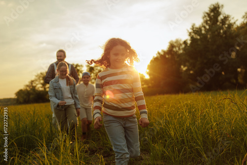 Obraz na plátně Family enjoying walking through meadow at sunset embracing sustainable living