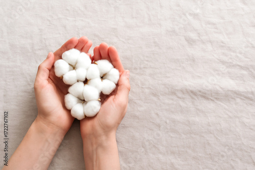 Photograph of hands gently holding raw cotton bolls above a rustic linen tablecloth, with ample copy space for modern banners, eco branding, or natural product presentations.