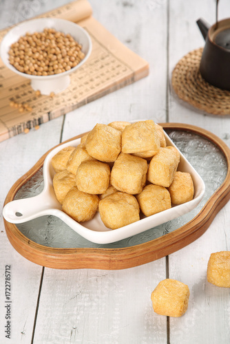 Golden Fried Tofu Puffs in White Dish with Soybeans on Wooden Background