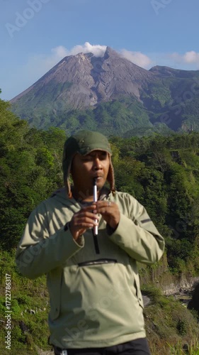 A male musician plays a traditional Irish instrument called a tin whistle against the backdrop of an active volcano. A tin whistle player shows off his skills in the wilderness on a sunny morning.