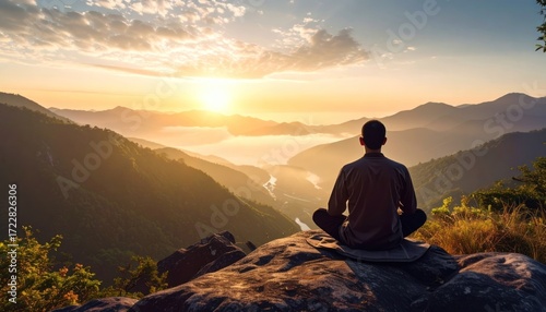Person meditates at dawn atop a rocky outcrop, overlooking valley; mountain silhouettes, sunlight
