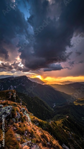 Dramatic sunset over lush, green mountains with a looming dark cloudscape, capturing a sense of impending weather and natural beauty