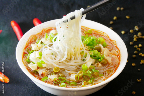 Close-up of a person picking up rice noodles with chopsticks, depth of field