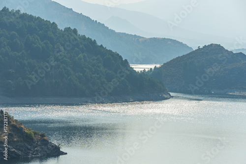 Panoramic view of the Atazar Reservoir at sunset, with blue waters surrounded by mountains and orange skies reflecting on the surface