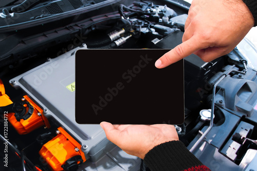 Mechanic using digital tablet with black blank screen to inspect hybrid or electric vehicle battery system, modern car maintenance with smart technology and EV diagnostics for performance