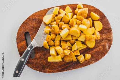 chopped baby potatoes on wooden board with knife on kitchen bench