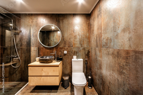 Modern bathroom with stone sink, toilet, wood vanity, and rustic tiles. Walk-in shower with glass partition enhances spa-inspired design, blending elegance, comfort, and contemporary wellness style.