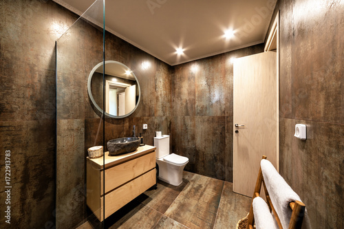 Contemporary bathroom featuring stone basin, sleek toilet, wooden vanity, rustic wall textures, and glass walk-in shower. Interior blends modern comfort, spa-like ambiance, and elegant architectural d