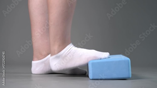 Individual balance training on a blue block with bare feet, demonstrating foot position and stability on a gray studio background