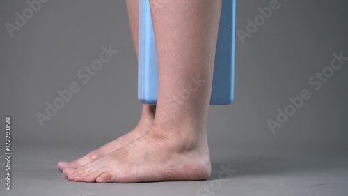 Individual balance training on a blue block with bare feet, demonstrating foot position and stability on a gray studio background
