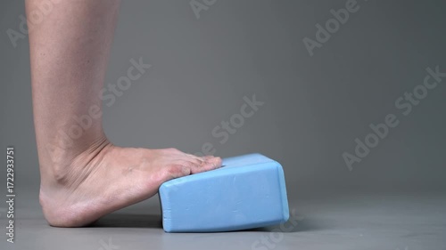 Individual balance training on a blue block with bare feet, demonstrating foot position and stability on a gray studio background