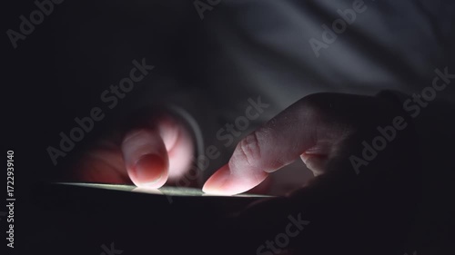 Extreme closeup of woman’s hands using mobile phone in low light, scrolling and searching online late at night.