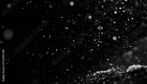 Abstract, monochrome image of particles suspended in air, softly illuminated from an angle, creating bokeh and depth against a dark background