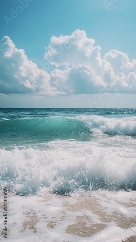 Rolling waves crash on a sandy shore under a bright, partly cloudy sky