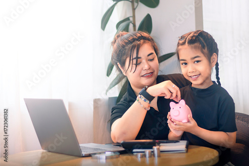 Fototapet Mother teaches daughter about saving money with a pink piggy bank at home during