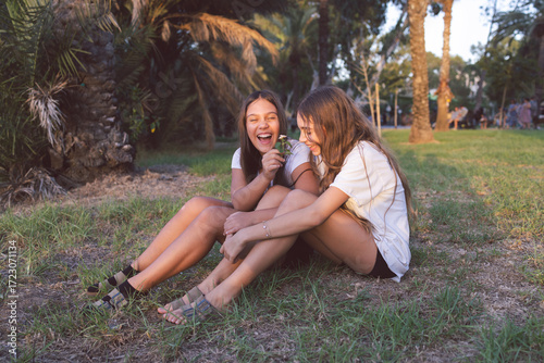 Portrait of two smiling teen girls sitting on the grass. Happy girlfriends enjoying themselves in the park