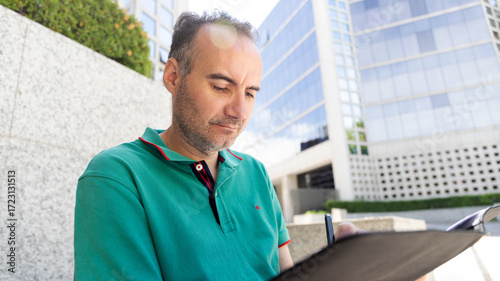 middle-aged man signing documents in front of a glass building
