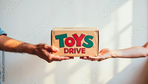Hands exchanging a box labeled 'TOYS DRIVE' in a bright room  