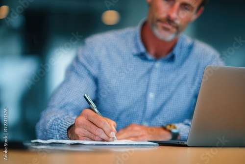 a businessman in a shirt is working on a laptop computer he taking notes or participating in a meeting in a conference room, using the laptop for a financial concept. the background is blurred.