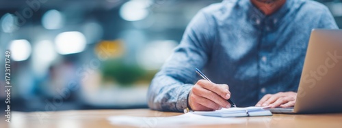 a businessman in a shirt is working on a laptop computer he taking notes or participating in a meeting in a conference room, using the laptop for a financial concept. the background is blurred.