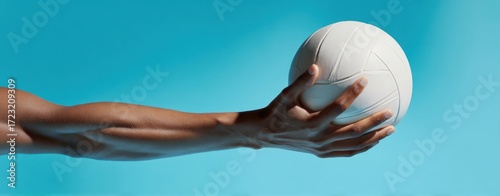 The Volleyball held by a fit arm against a vibrant blue studio backdrop