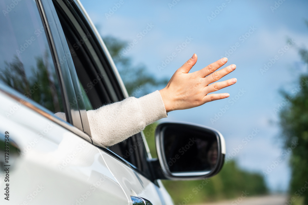 Naklejka premium A hand extending out of a car window making a gesture, likely indicating or signaling while on a road trip outdoors.