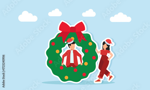 A woman in red outfit with Christmas hat stands near a man in red outfit with Christmas hat appearing from a circular wreath illustration for Christmas celebration