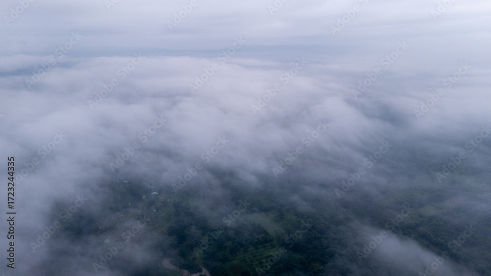 Fototapeta premium Aerial of Village in rain cloud cover tropical green mountain. Rainy season. Misty cover green forest. beautiful green village