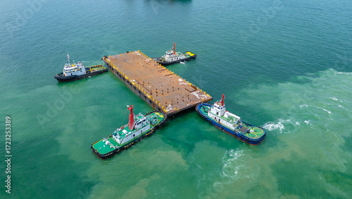Foto Aerial view of tugboats towing a large rusty steel barge in the ocean, used for transporting heavy industrial cargo or offshore construction