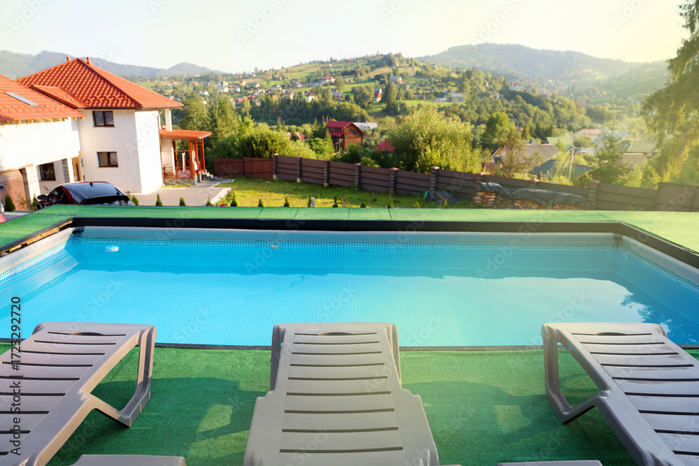 Obraz premium Empty sun loungers on artificial grass near outdoor swimming pool