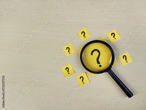 Question sign on note paper with magnifying glass on wooden table background, Search for solutions concept. Flat lay 