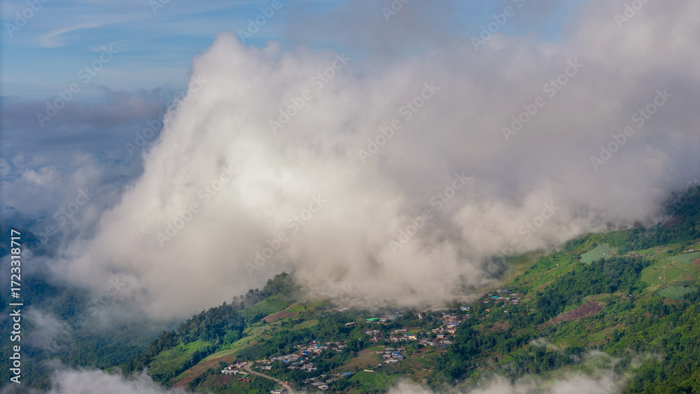 Fototapeta premium Aerial of Village in rain cloud cover tropical green mountain. Rainy season. Misty cover green forest. beautiful green village
