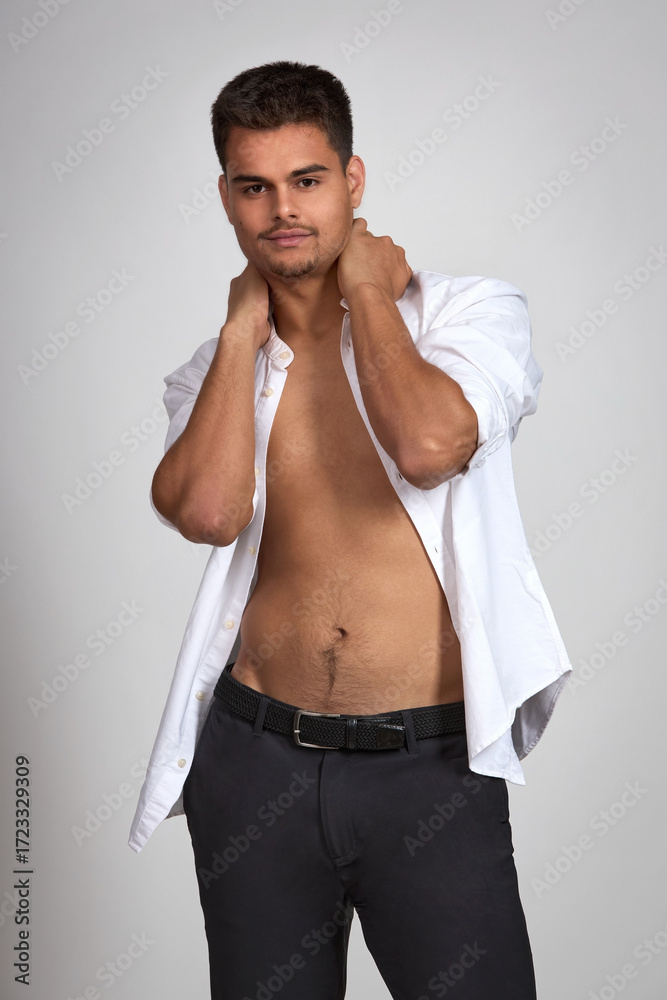 Fototapeta premium Attractive young brunette guy with short haircut in black trousers and white shirt posing in studio on white background