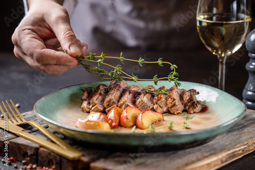 Chef plating gourmet duck breast with herbs