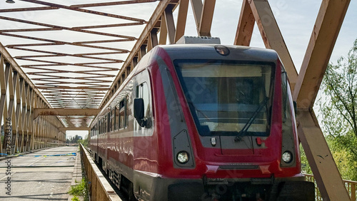 Foto Red train journeys through lattice bridge shadows, embodying steely wanderlust a
