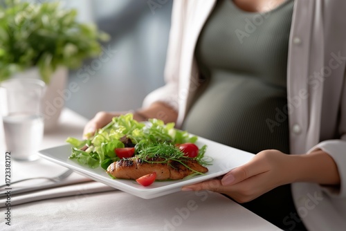 Pregnant woman holding a plate with grilled fish and fresh salad, showcasing healthy eating habits and nurturing lifestyle in a cozy dining setting