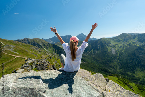 Hiking woman on mountain peak looking in beautiful mountain valley in summer. Landscape with sporty young woman.