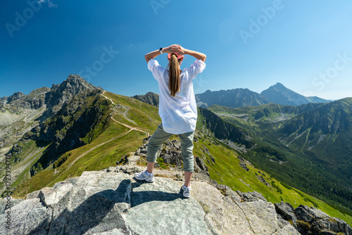 Hiking woman on mountain peak looking in beautiful mountain valley in summer. Landscape with sporty young woman.