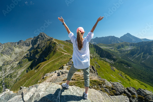 Hiking woman on mountain peak looking in beautiful mountain valley in summer. Landscape with sporty young woman.